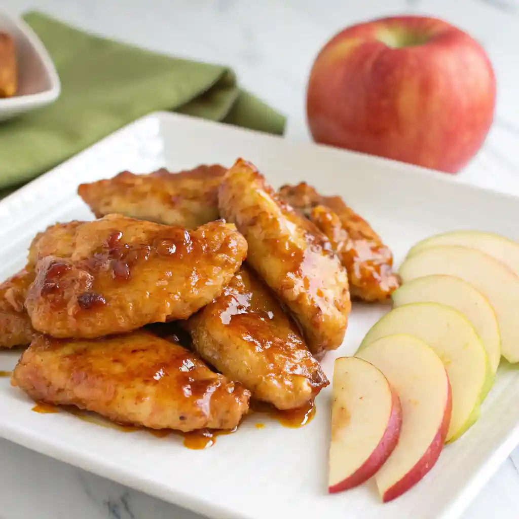 Apple and Honey-Glazed Chicken Tenders on a white plate with a glossy glaze and apple slices.