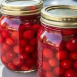 Homemade canned cherries preserved in mason jars filled with vibrant red fruit and syrup, neatly arranged on a kitchen surface.