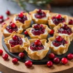 A plate of cranberry and goat cheese phyllo cups garnished with fresh cranberries and rosemary on a wooden board.