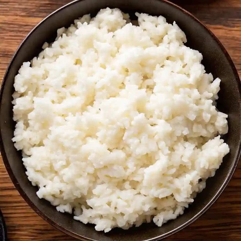 Side view of sticky sushi rice in a bowl with a gentle steam rising.
