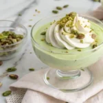 Overhead shot of creamy pistachio pudding in a glass cup topped with whipped cream and chopped pistachios
