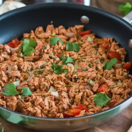 A flavorful Ground Chicken Recipe in a pan, cooked with onions, garlic, tomatoes, and spices, garnished with fresh herbs on a wooden board.