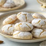 Ricciarelli Italian almond cookies on a vintage gold-rimmed plate with powdered sugar and cracked tops.