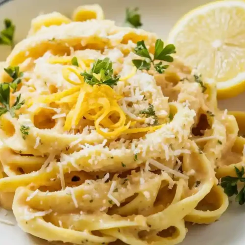 Plate of Lemon Parmesan Pasta with lemon zest, parsley, and a lemon wedge, served on a wooden board.