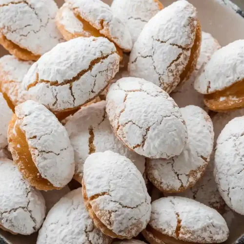 Ricciarelli honey recipe cookies, almond-shaped, cracked on top, and dusted with powdered sugar on a marble surface.