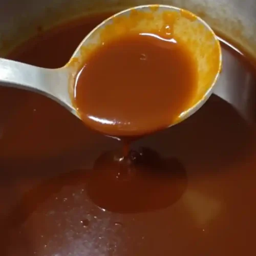 A pot of simmering golden demi-glace recipe with a rich, glossy texture.