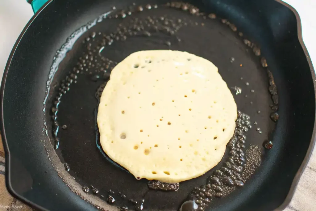 Pancake cooking in a hot skillet with bubbles forming on the surface.