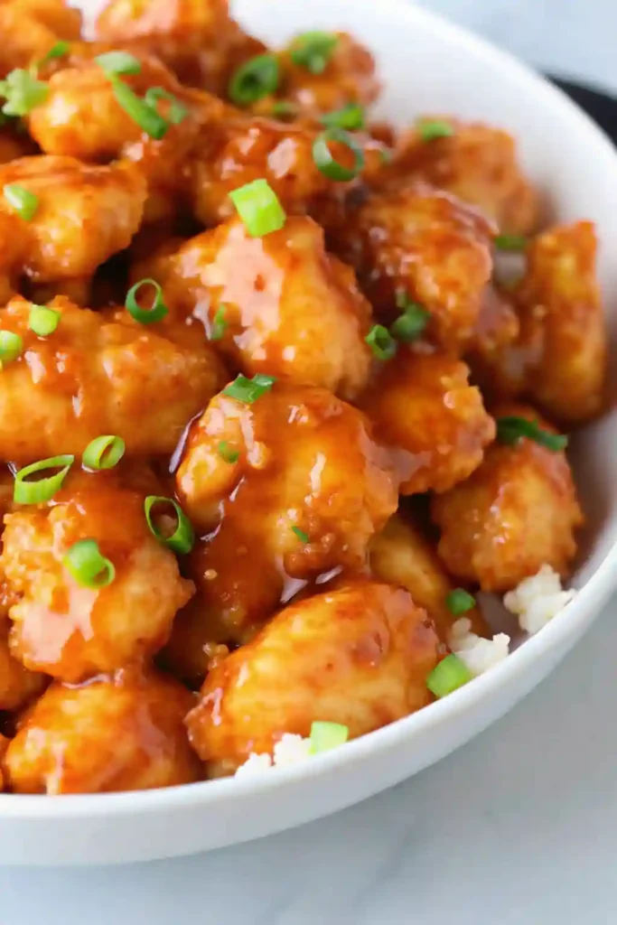 Close-up of Chinese orange chicken recipe served over white rice and topped with chopped green onions