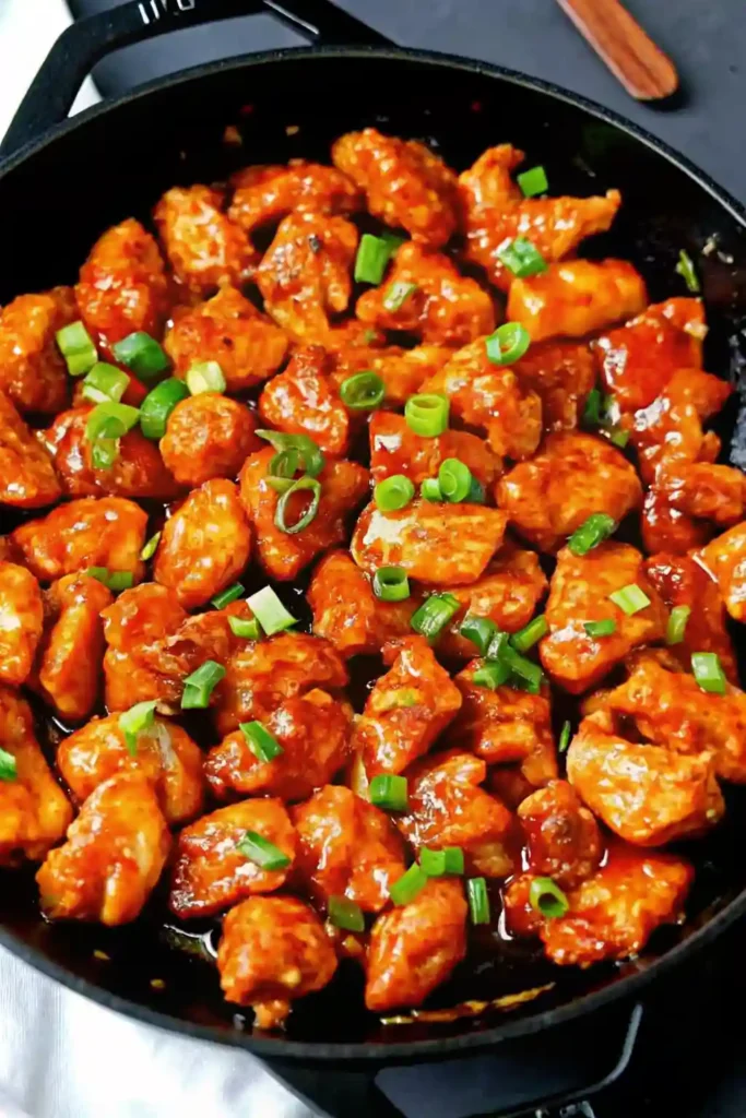 Skillet filled with homemade orange chicken coated in glossy sauce and topped with chopped green onions
