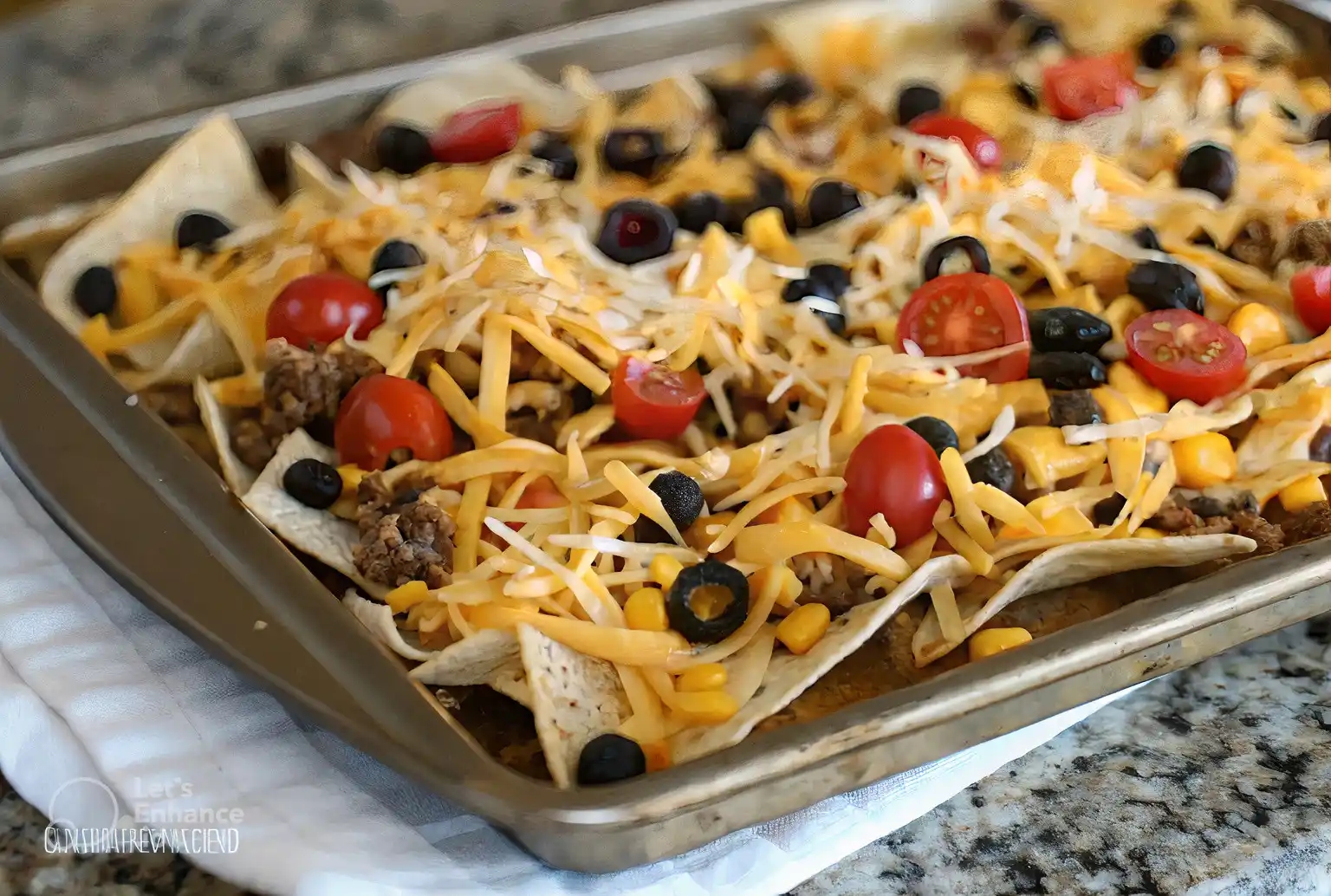 Sheet pan nachos topped with shredded cheese, cherry tomatoes, black olives, corn, and seasoned ground beef on a baking tray.