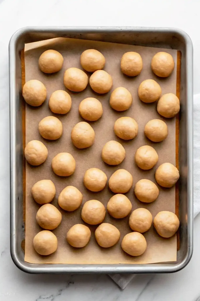 Uncoated peanut butter balls arranged on a parchment lined baking sheet before chilling.