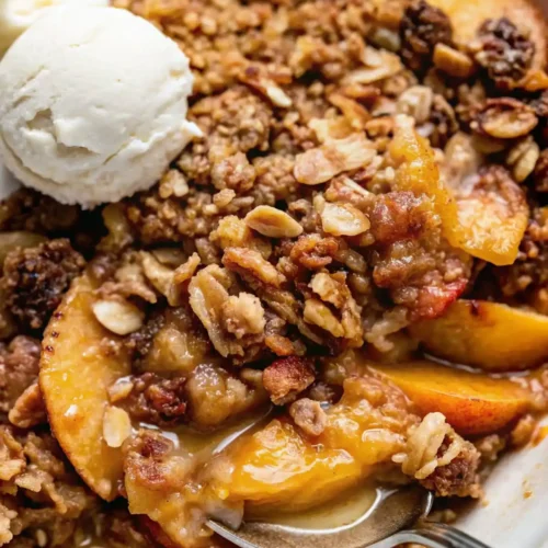 Warm peach crisp with juicy peach slices, crunchy oat topping, and melting vanilla ice cream with a spoon scooping the filling.