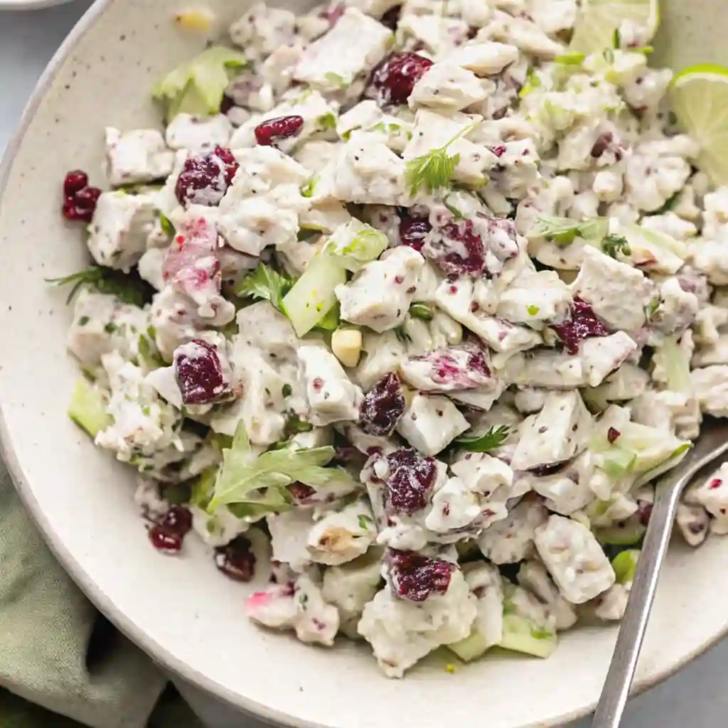 Healthy chicken salad with dried cranberries, celery, and herbs in a white bowl