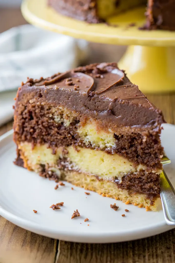 Slice of homemade marble cake with chocolate frosting on a white plate