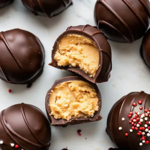 Chocolate covered peanut butter balls with one ball showing a bitten center and others topped with red and white sprinkles.