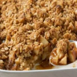 Golden apple crisp with oat topping in a white baking dish, served warm with caramelized apple filling visible