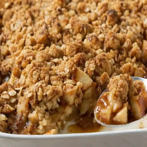 Golden apple crisp with oat topping in a white baking dish, served warm with caramelized apple filling visible
