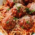 Close-up of spaghetti topped with homemade Italian meatballs in tomato sauce, garnished with Parmesan and fresh basil.