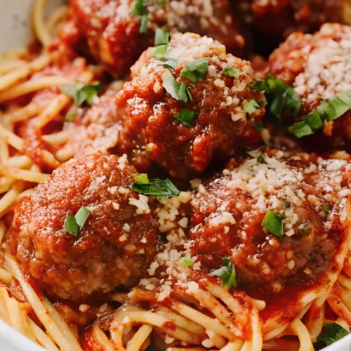 Close-up of spaghetti topped with homemade Italian meatballs in tomato sauce, garnished with Parmesan and fresh basil.