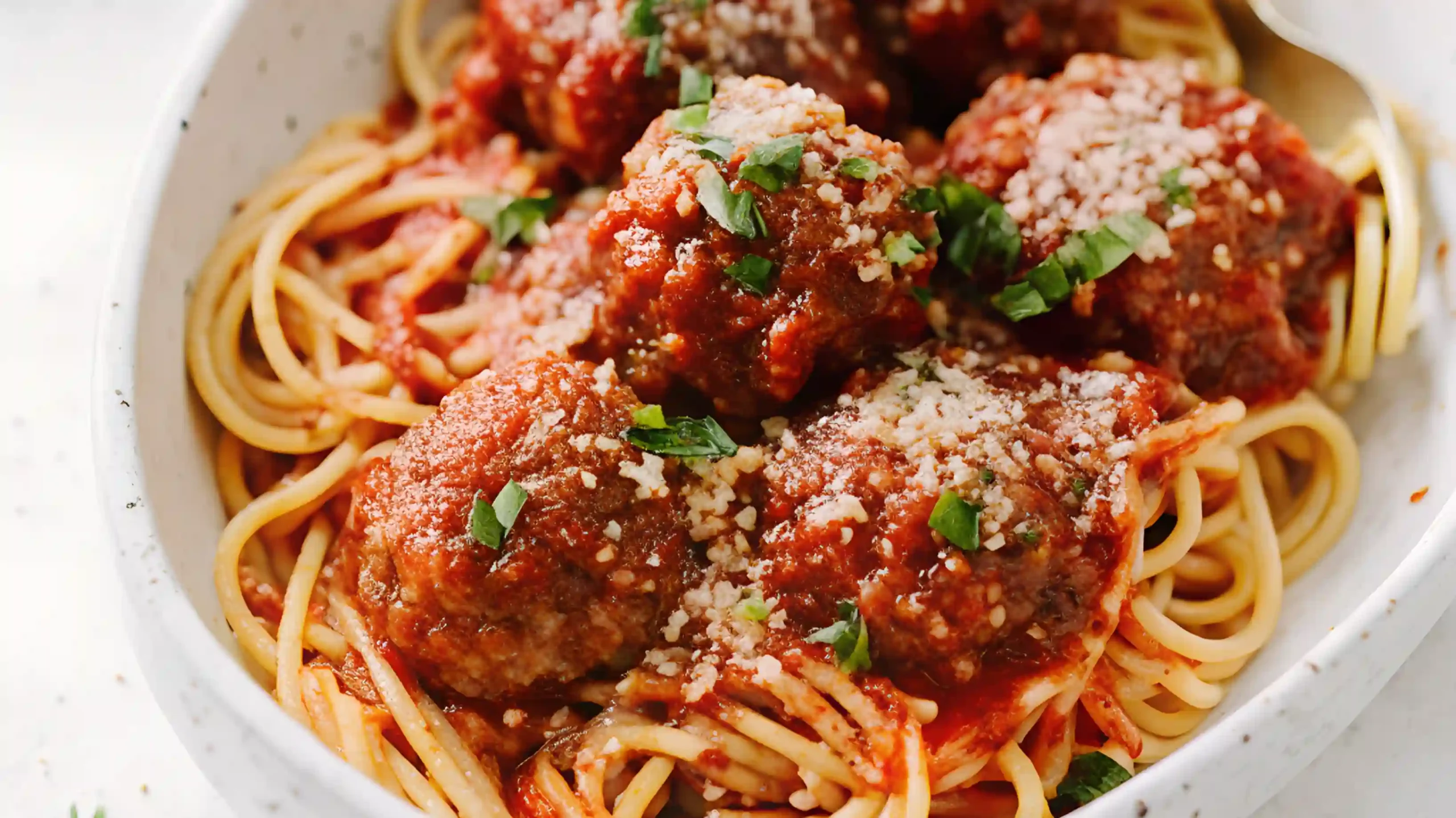 Close-up of spaghetti topped with homemade Italian meatballs in tomato sauce, garnished with Parmesan and fresh basil.