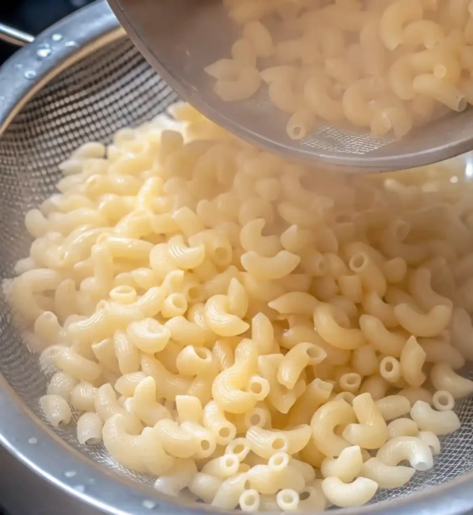 Steaming elbow macaroni being poured into a strainer after boiling.