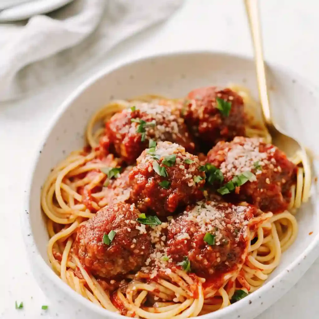 Bowl of spaghetti topped with homemade meatballs, marinara sauce, grated Parmesan, and fresh parsley.