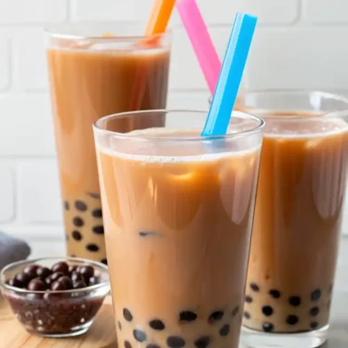 Three tall glasses of iced milk tea with chewy tapioca pearls and colorful wide straws.