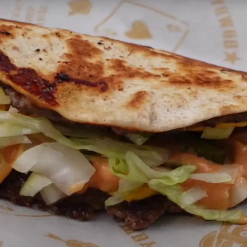 Smash burger taco with melted cheese, pickles, lettuce, onions, and burger sauce in a toasted tortilla.