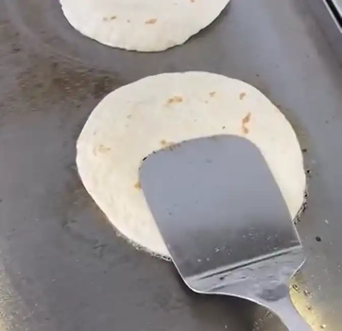 Flour tortillas being flipped on a griddle while cooking for smash burger tacos.