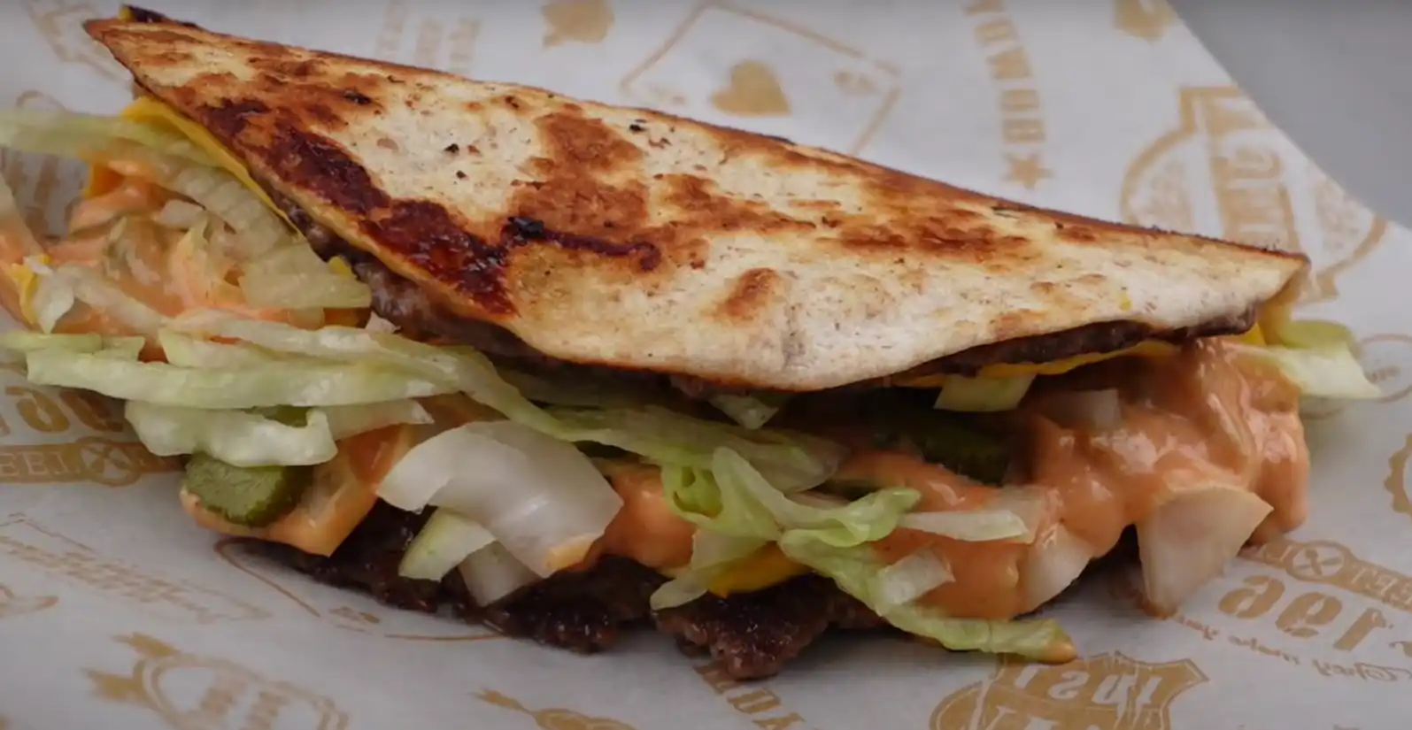 Smash burger taco with melted cheese, pickles, lettuce, onions, and burger sauce in a toasted tortilla.