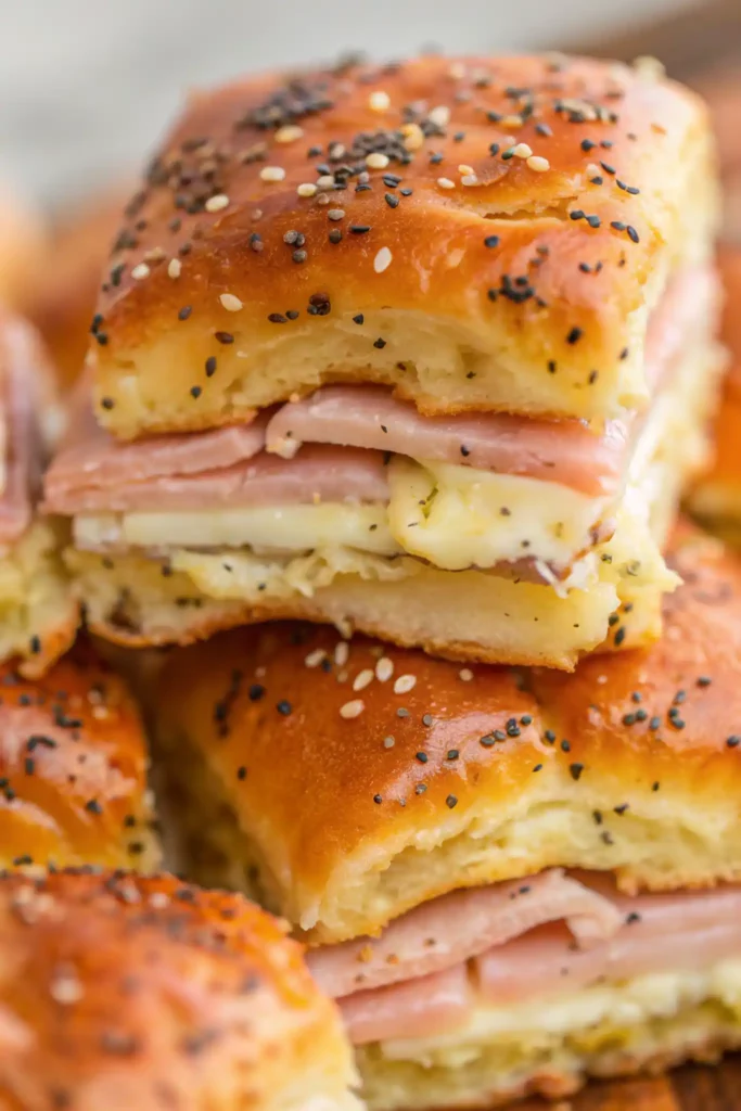 Stacked ham and cheese sliders with golden Hawaiian rolls topped with poppy and sesame seeds
