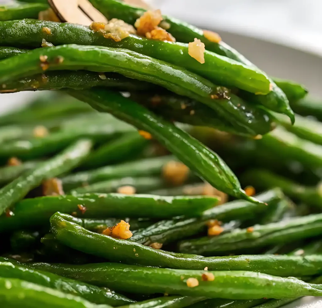 Close-up of sautéed green beans topped with golden garlic bits.