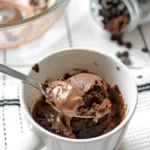 Fudgy chocolate mug cake with a spoon lifting a gooey melted chocolate bite from a white mug.