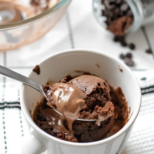 Fudgy chocolate mug cake with a spoon lifting a gooey melted chocolate bite from a white mug.