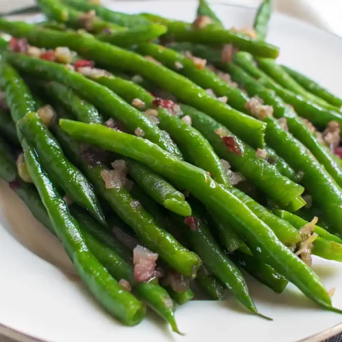 Bright green sautéed green beans topped with finely minced garlic on a white plate.