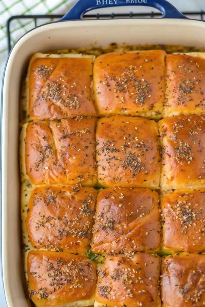 Hot ham and cheese sliders baked in a dish with golden tops sprinkled with sesame and herb seasoning