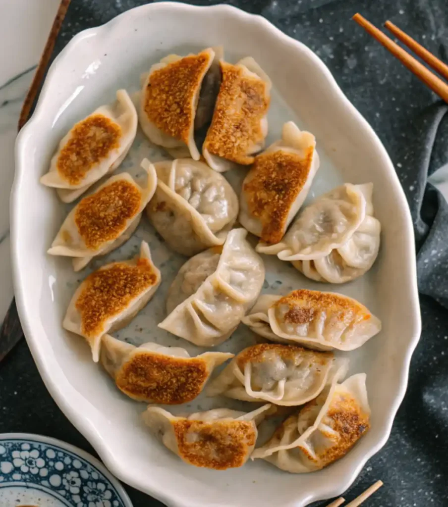Pan-fried dumplings arranged on a white ceramic plate with crispy golden bottoms and pleated edges.