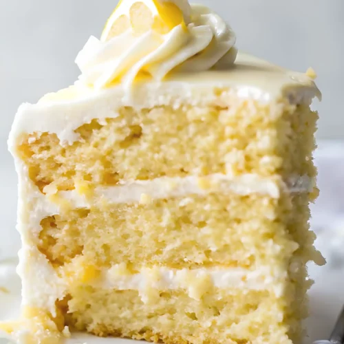 Slice of lemon layer cake with creamy frosting and a lemon swirl on top.