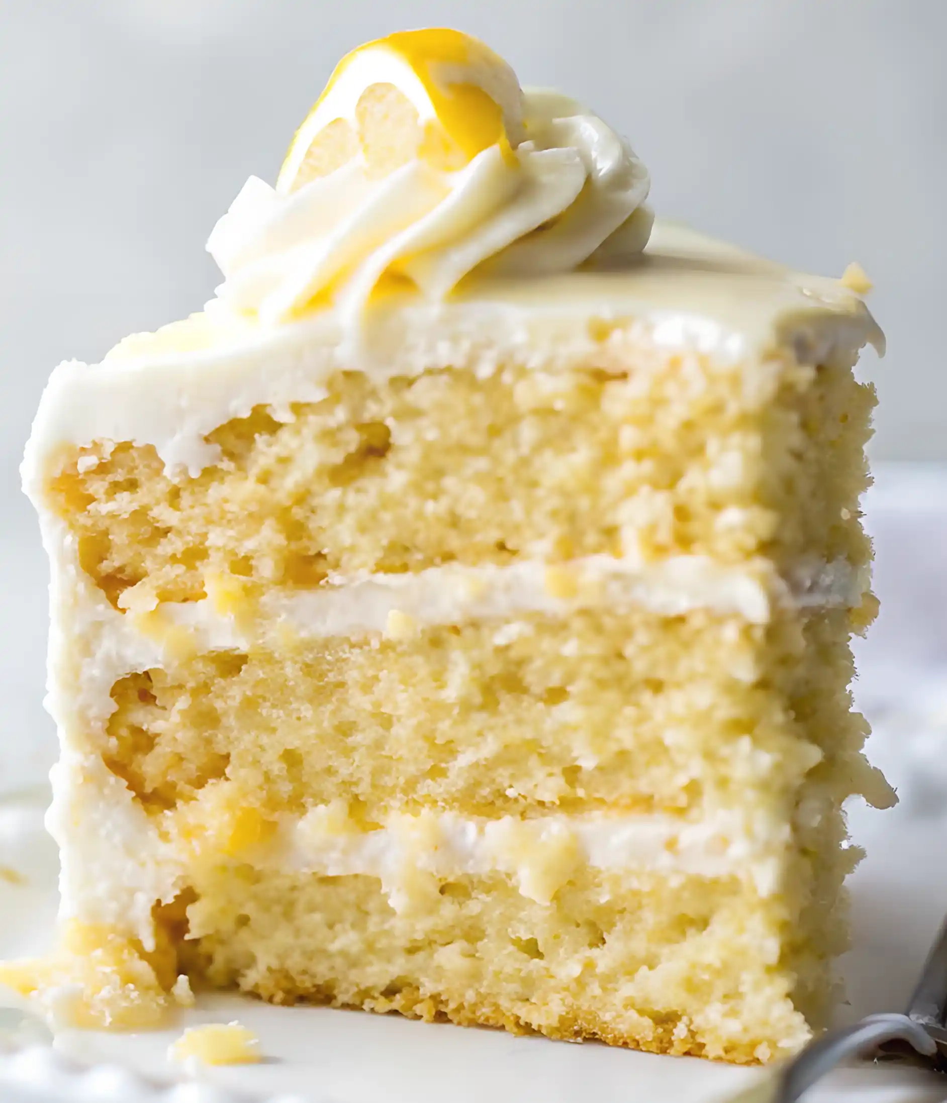 Slice of lemon layer cake with creamy frosting and a lemon swirl on top.