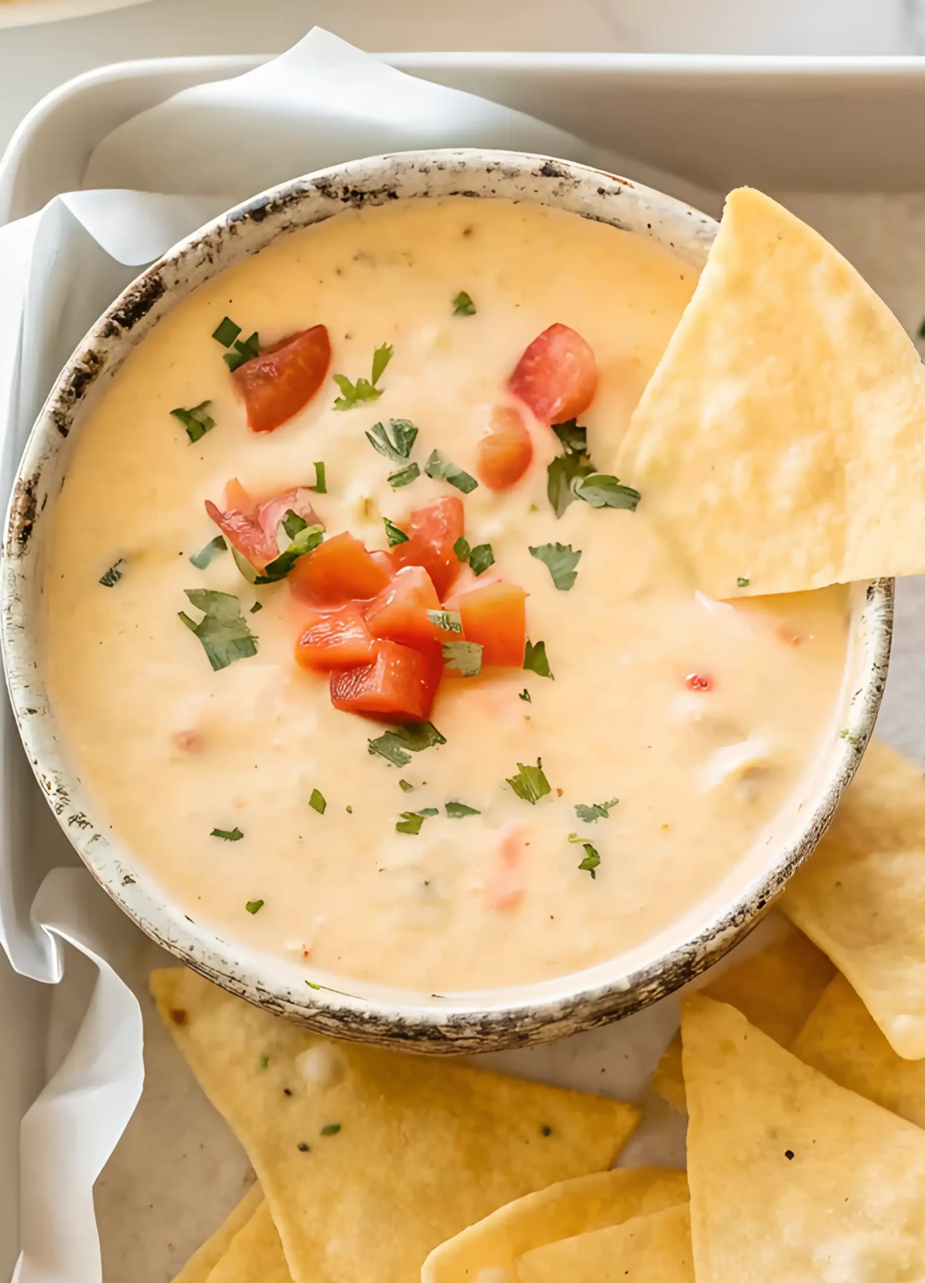 Creamy queso dip in a rustic bowl topped with diced tomatoes and cilantro, served with tortilla chips on the side.
