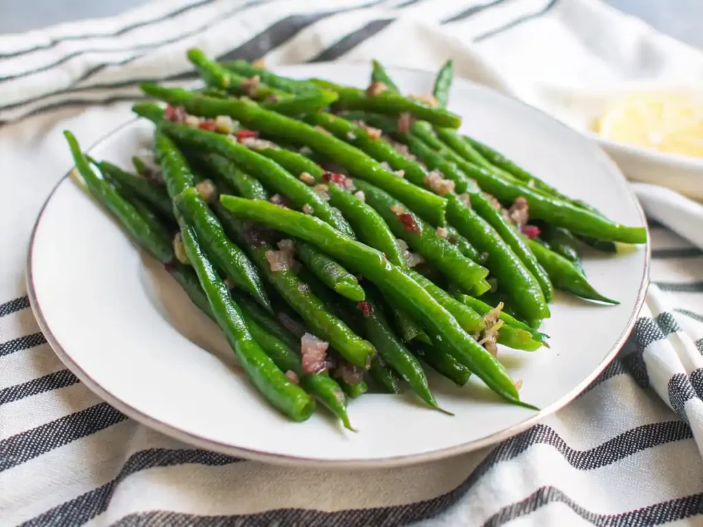 Plate of sautéed green beans topped with minced garlic and seasoning on a striped cloth.