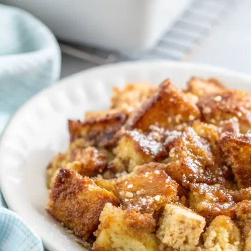 Slice of French toast casserole with caramelized bread cubes and cinnamon syrup served on a white plate.
