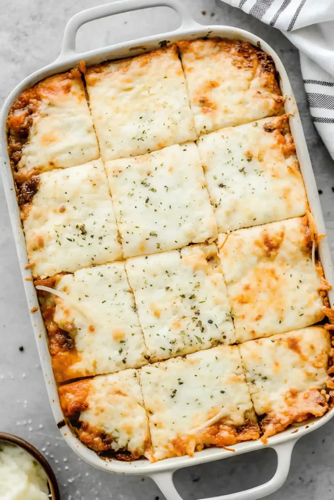 Freshly baked million dollar spaghetti casserole in a white rectangular dish, topped with golden melted cheese and sprinkled with herbs.