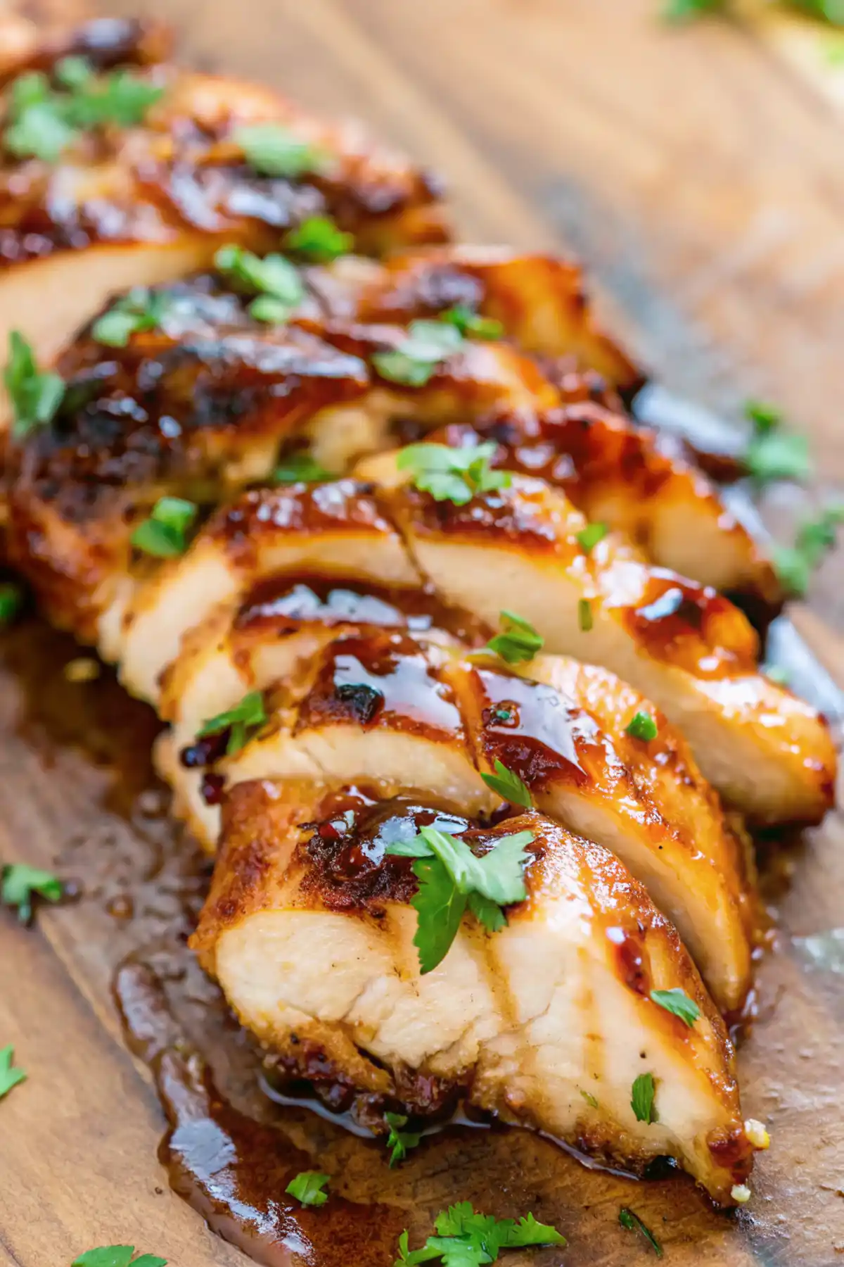 Sliced grilled chicken breast with glossy marinade and fresh parsley on wooden board