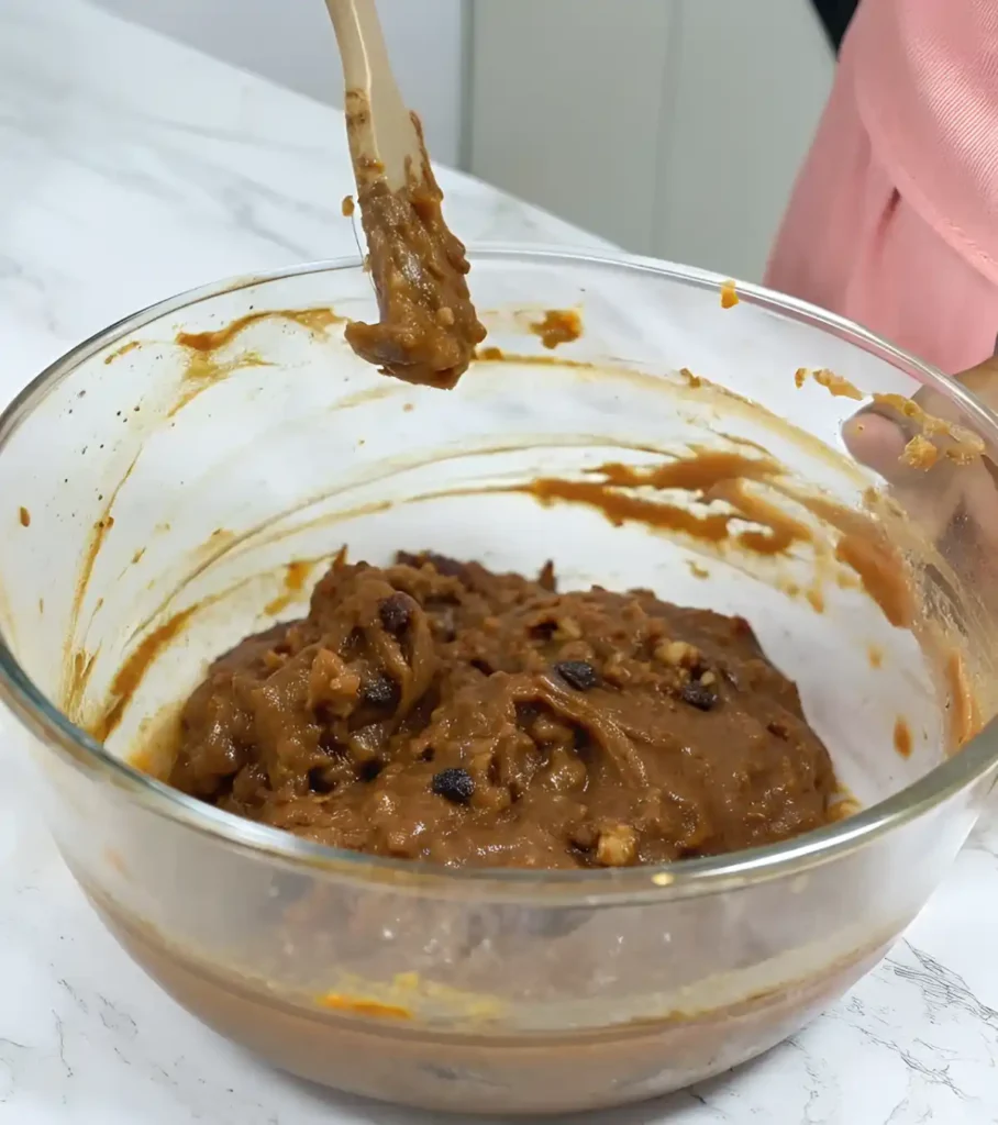 Glass bowl with thick fruit cake batter and a spatula holding a scoop mid-air