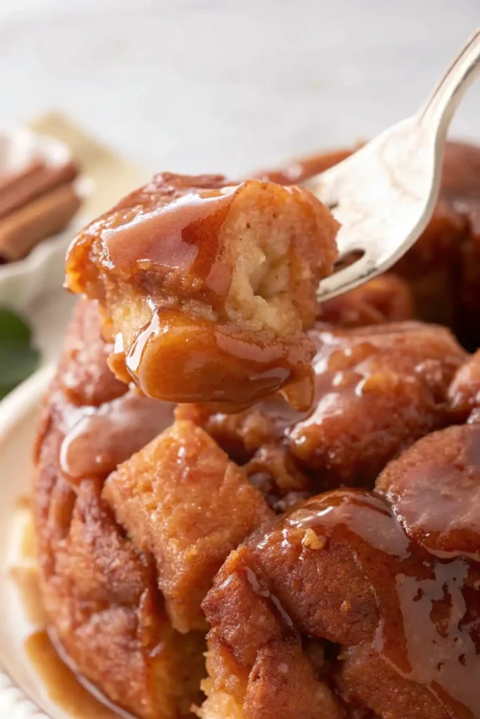 Fork lifting a gooey bite of easy monkey bread, coated in rich caramel glaze with cinnamon layers visible inside.