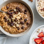 Bowl of chocolate oatmeal topped with sliced almonds, chocolate chips, and raisins