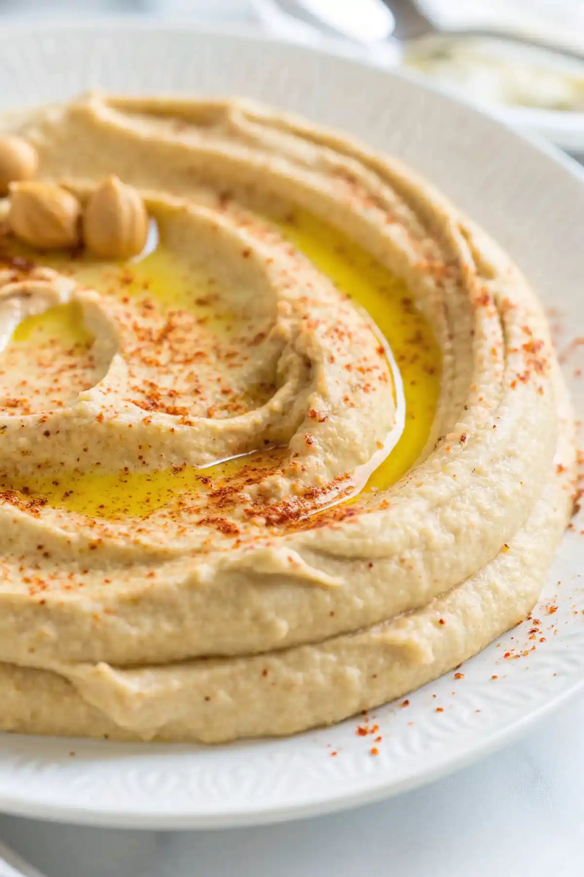 Smooth homemade hummus topped with olive oil, paprika, and chickpeas on a white plate