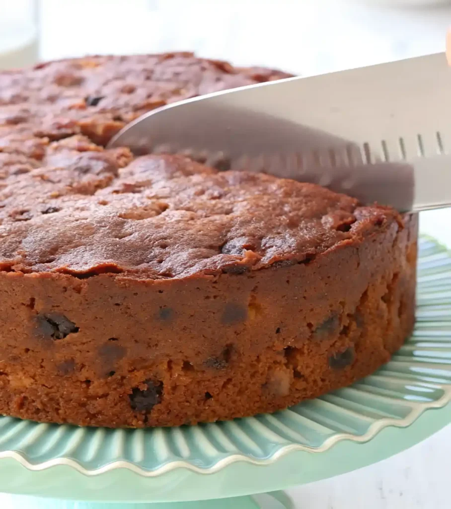 Whole fruit cake on a pastel stand being sliced with a large knife