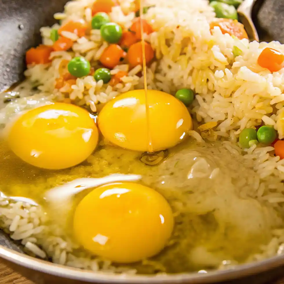 Raw eggs added to rice with peas and carrots in a skillet